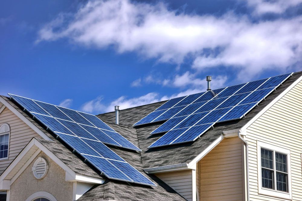 Solar panels installed on a suburban house roof under a blue sky with clouds