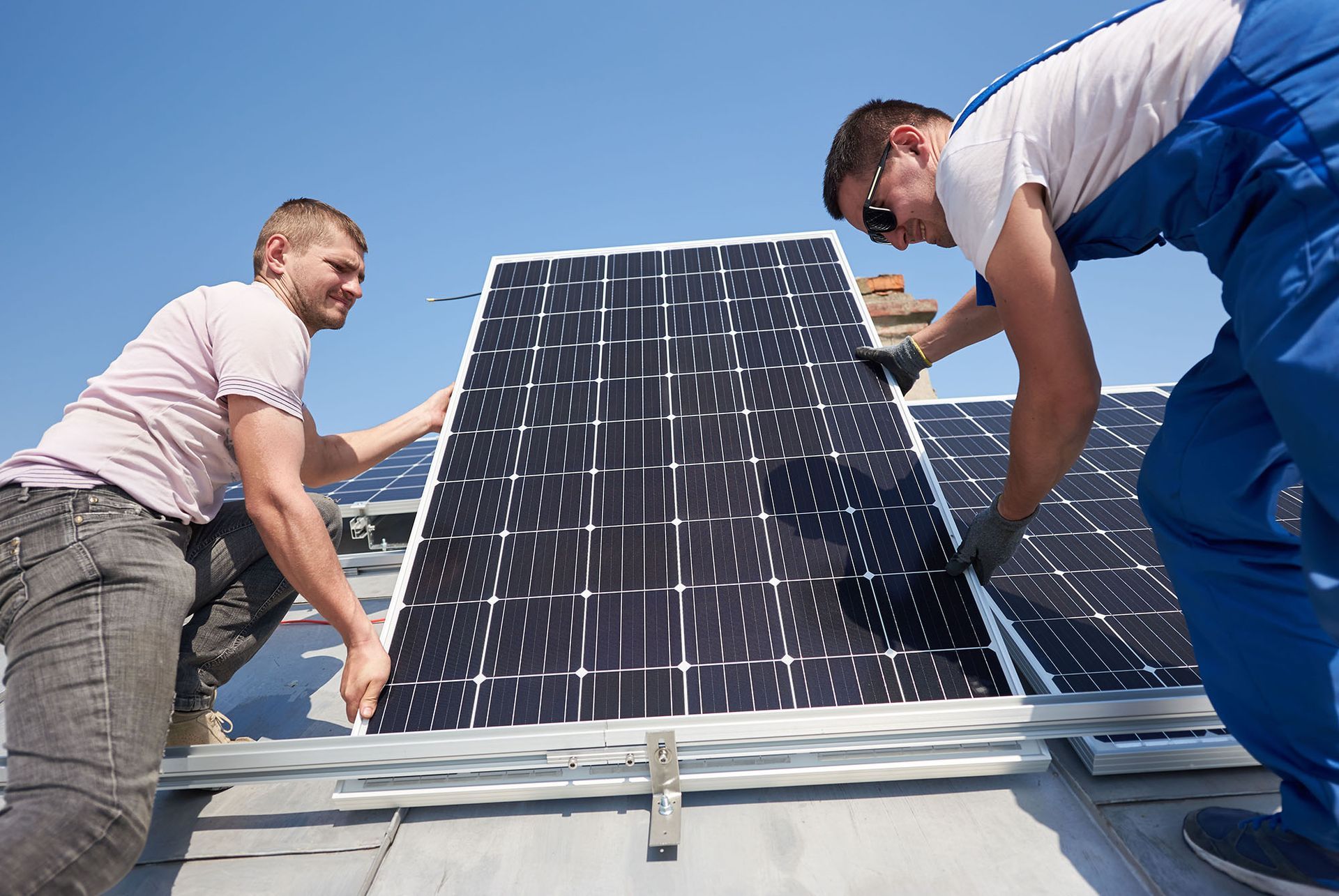 Two workers installing a solar panel on a rooftop under a blue sky