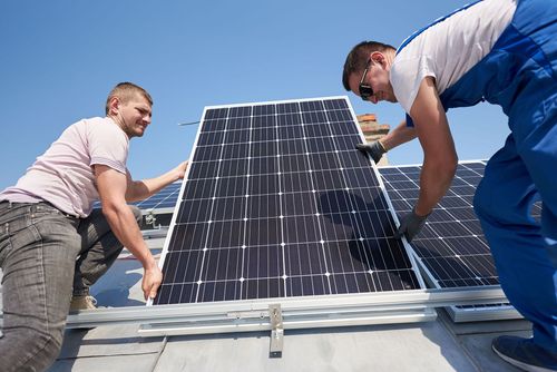 Two workers installing a solar panel on a rooftop under a blue sky