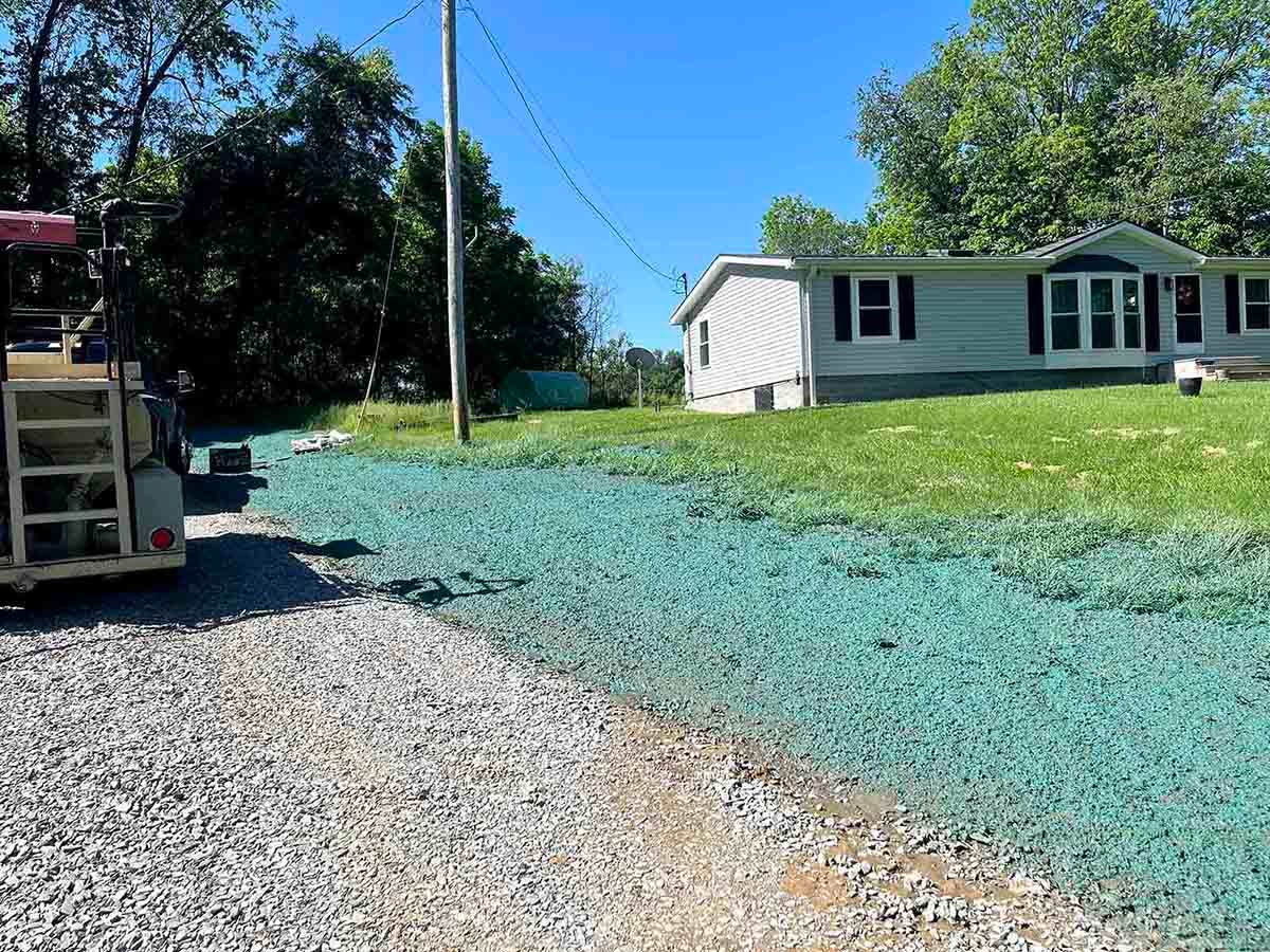 Gravel driveway beside a white house with green lawn under hydroseeding process