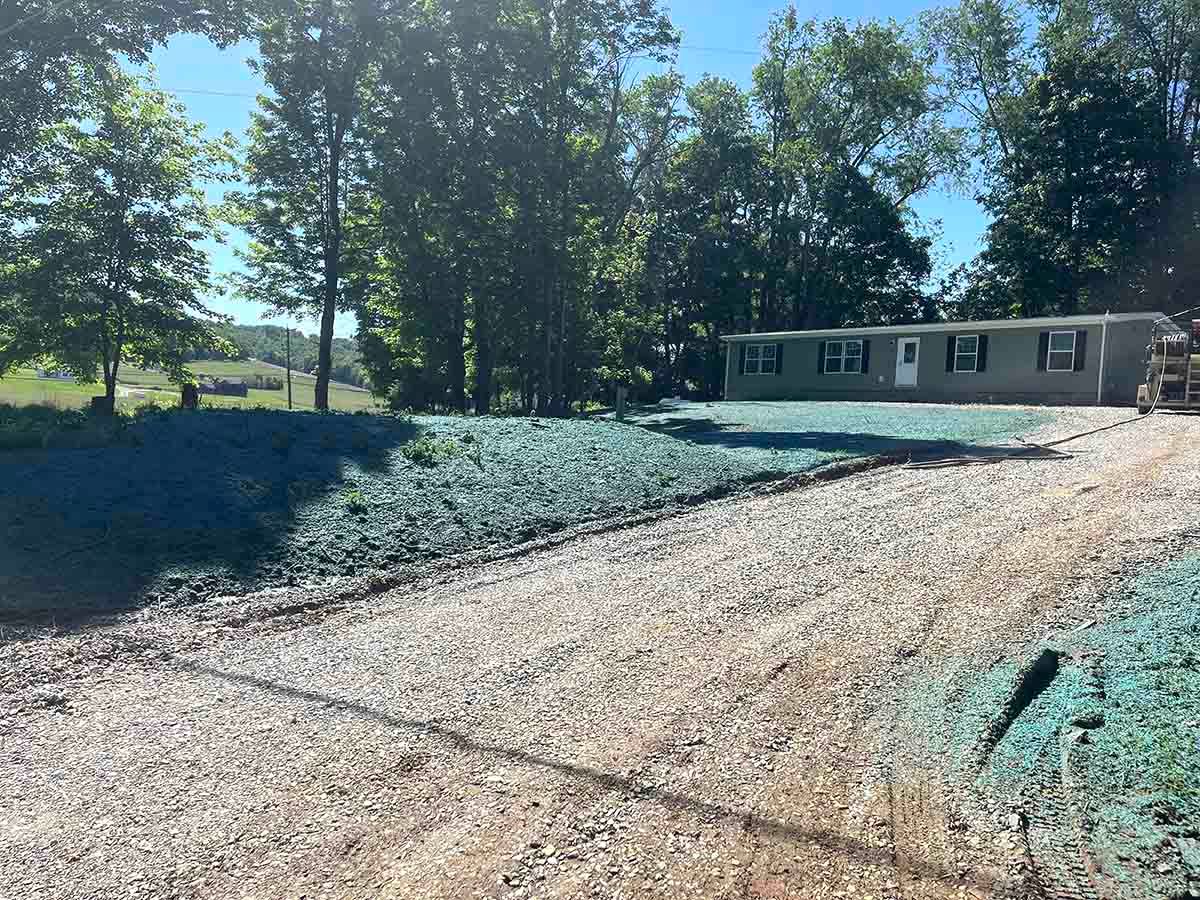 Gravel driveway leading to a house with a yard under hydroseeding process