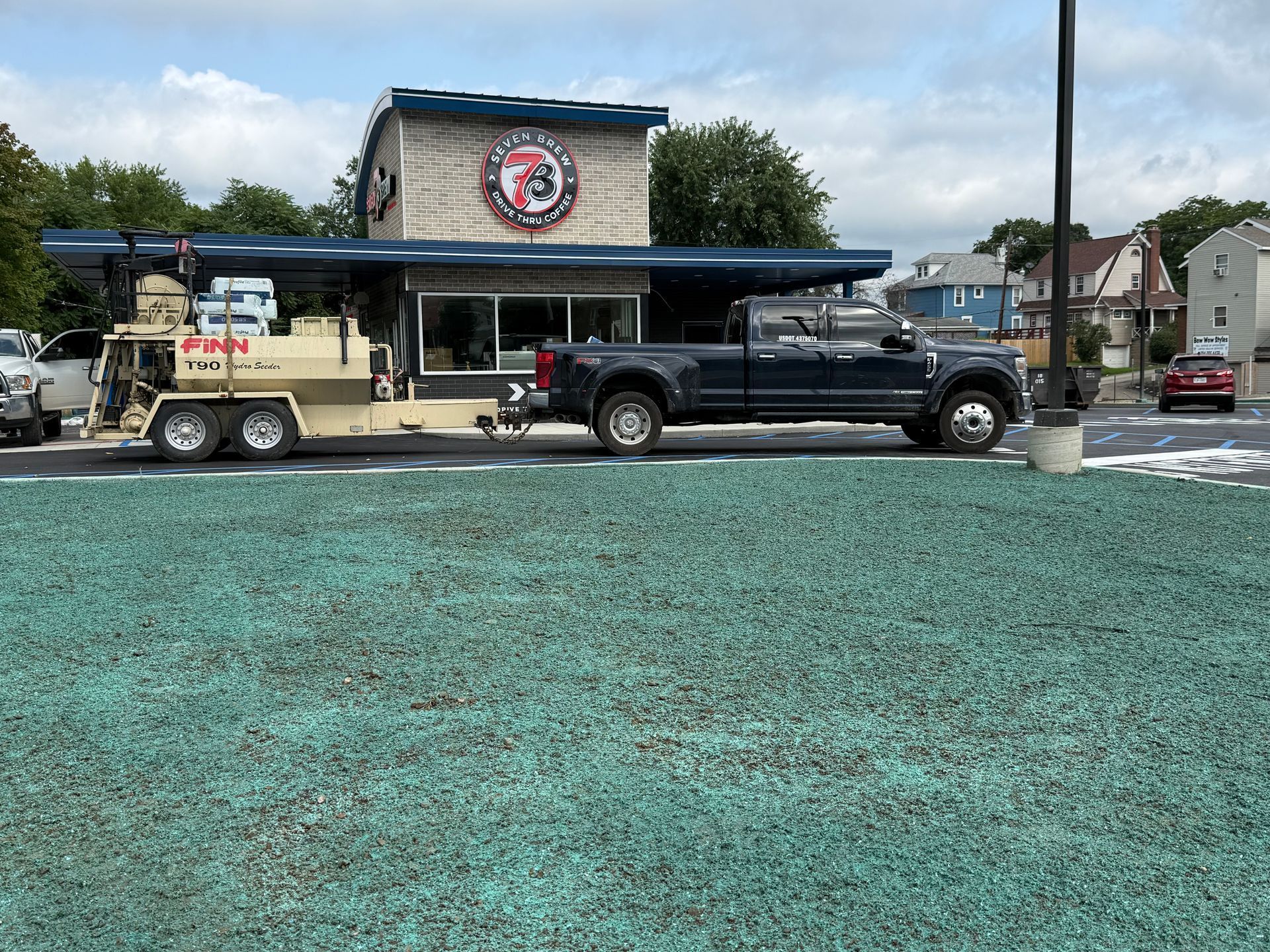 Black pickup and trailer parked outside a building with a circular logo, on a gravel lot under a cloudy sky