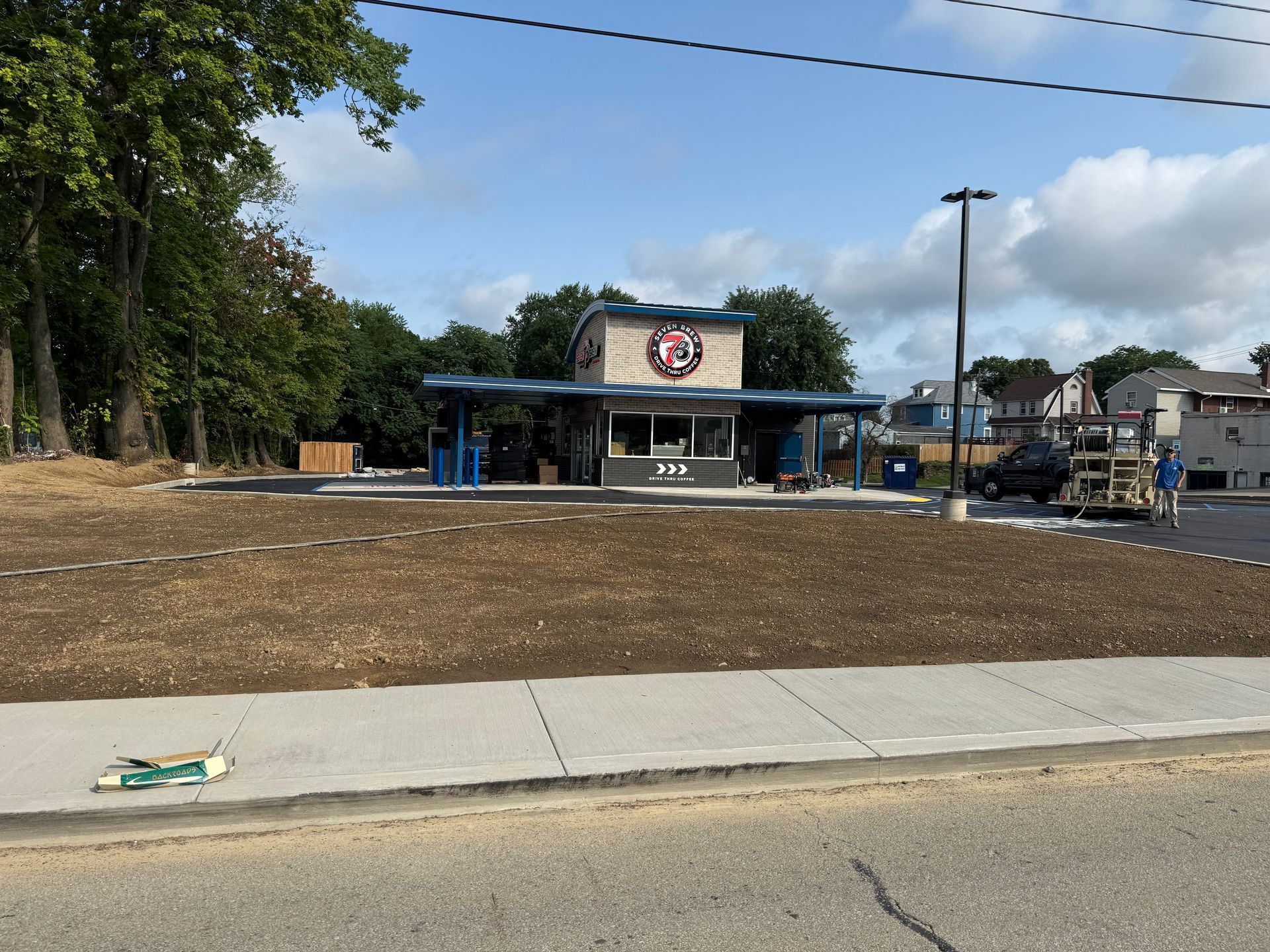 Empty lot with a small blue-roofed storefront or pavilion and a sign, seen across a sidewalk and road.