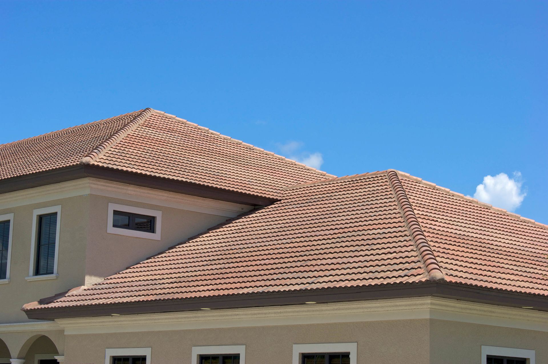 Modern house with a beige exterior and a red clay tile roof under a clear blue sky.