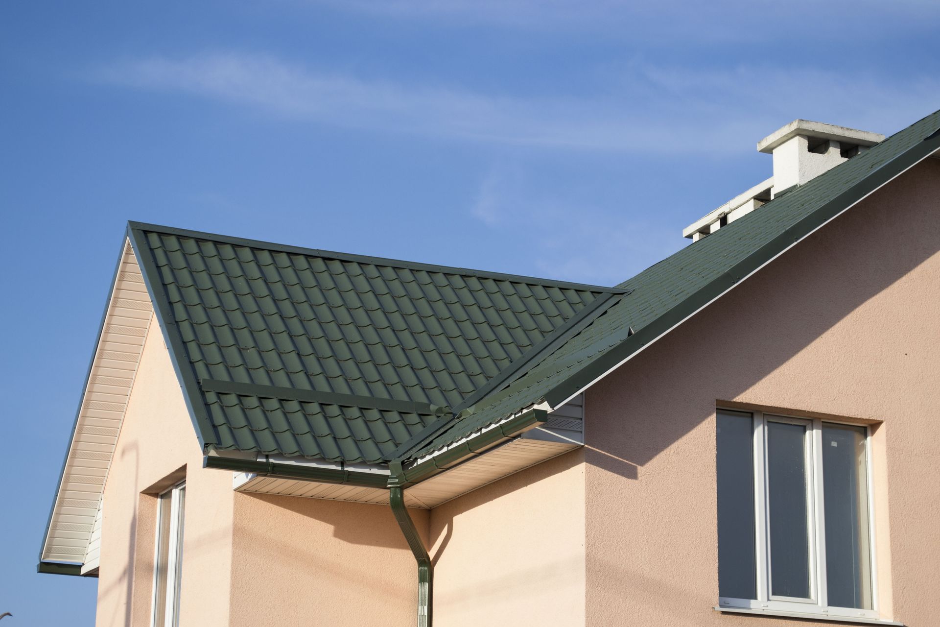 Modern house with a green metal tile roof and beige exterior walls on a sunny day.