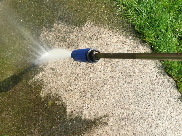 Garden hose spraying water on a concrete sidewalk beside grass