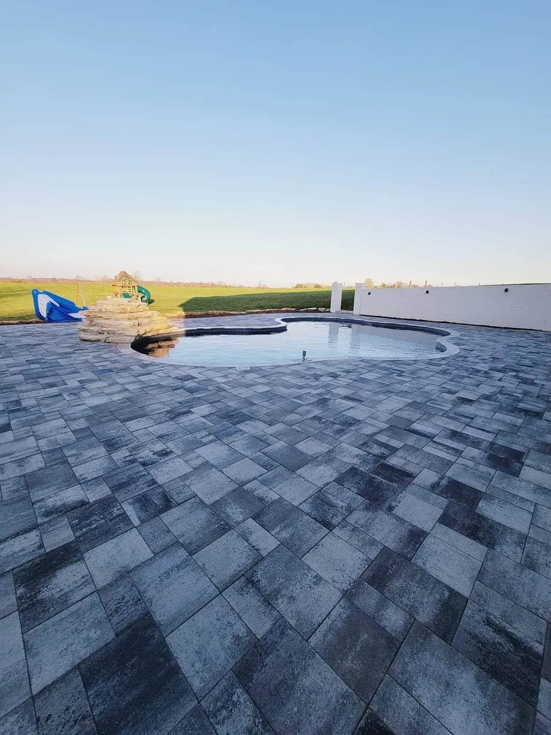 Rooftop terrace with gray pavers, low white walls, and a small pool under a clear sky.