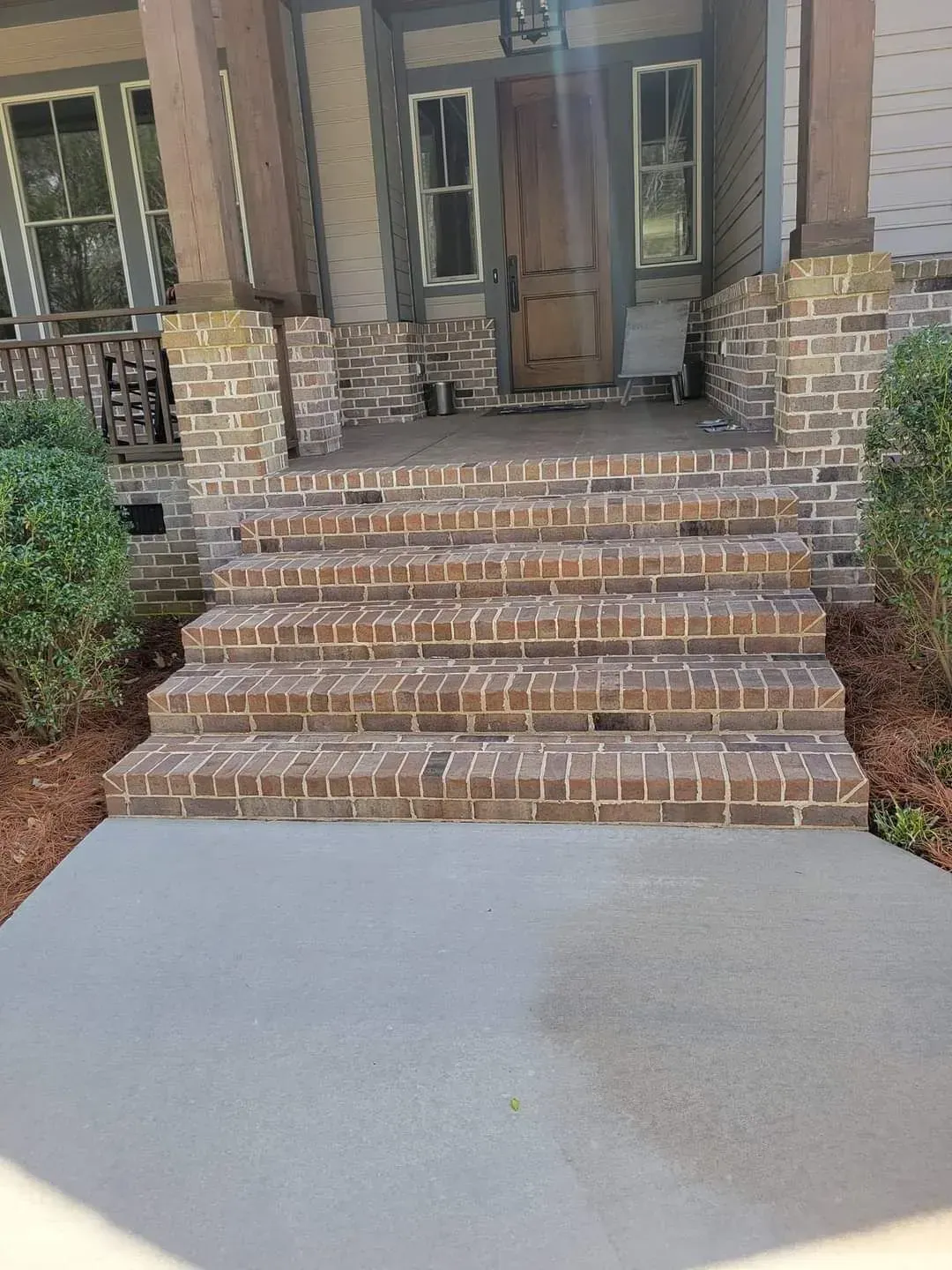 Brick front steps leading to a porch entrance with stone columns and a concrete walkway
