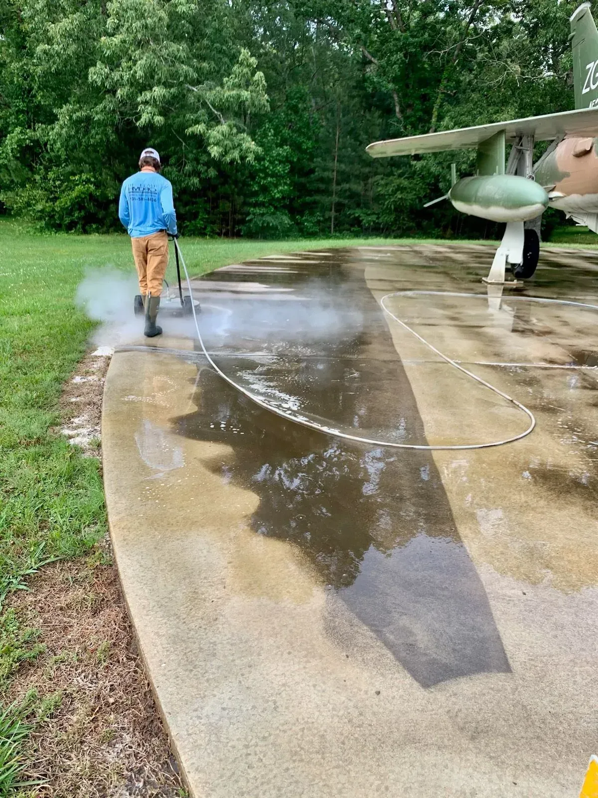 Person walking on a wet driveway beside a small airplane, with a hose lying across the concrete.