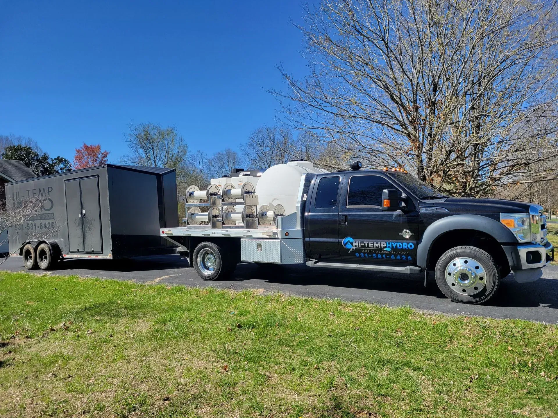 Black utility truck towing a trailer parked on a roadside under a clear blue sky