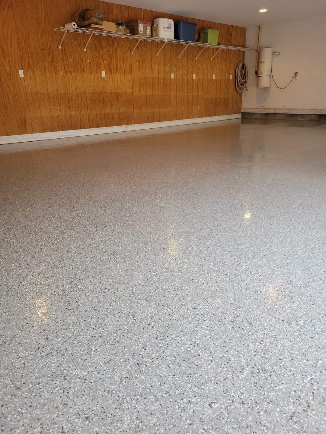 Empty garage with a speckled gray floor and a wooden wall-mounted workbench at the back.