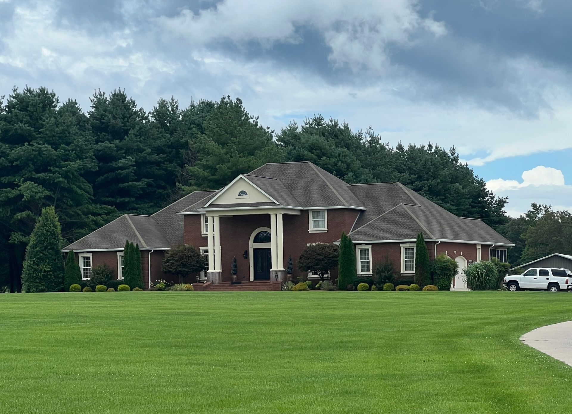 Large brick house with white columns on a green lawn under a cloudy sky