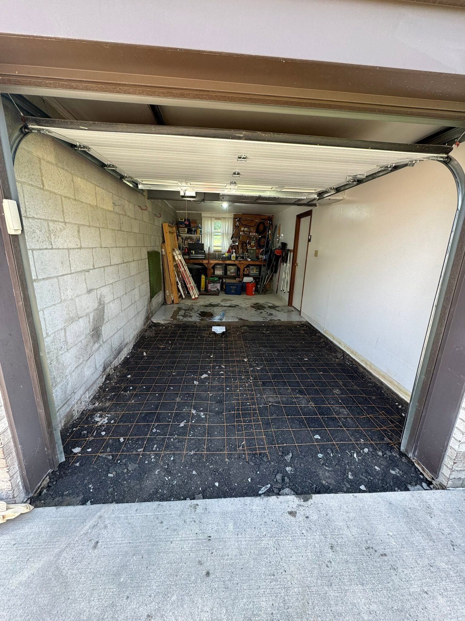 Empty garage with a dark floor covering, white walls, and storage items at the back.