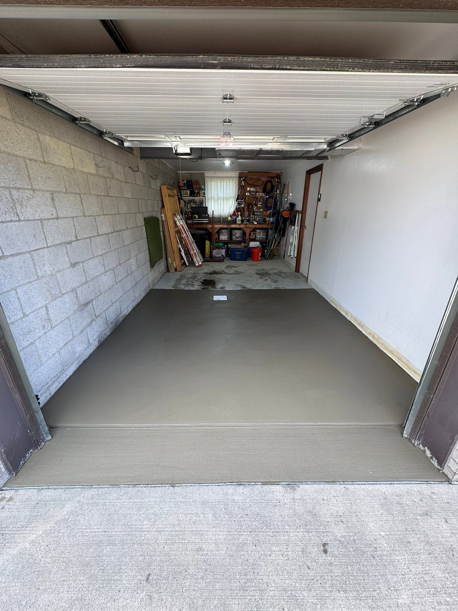 Open garage with white walls, gray floor, and storage items at the back