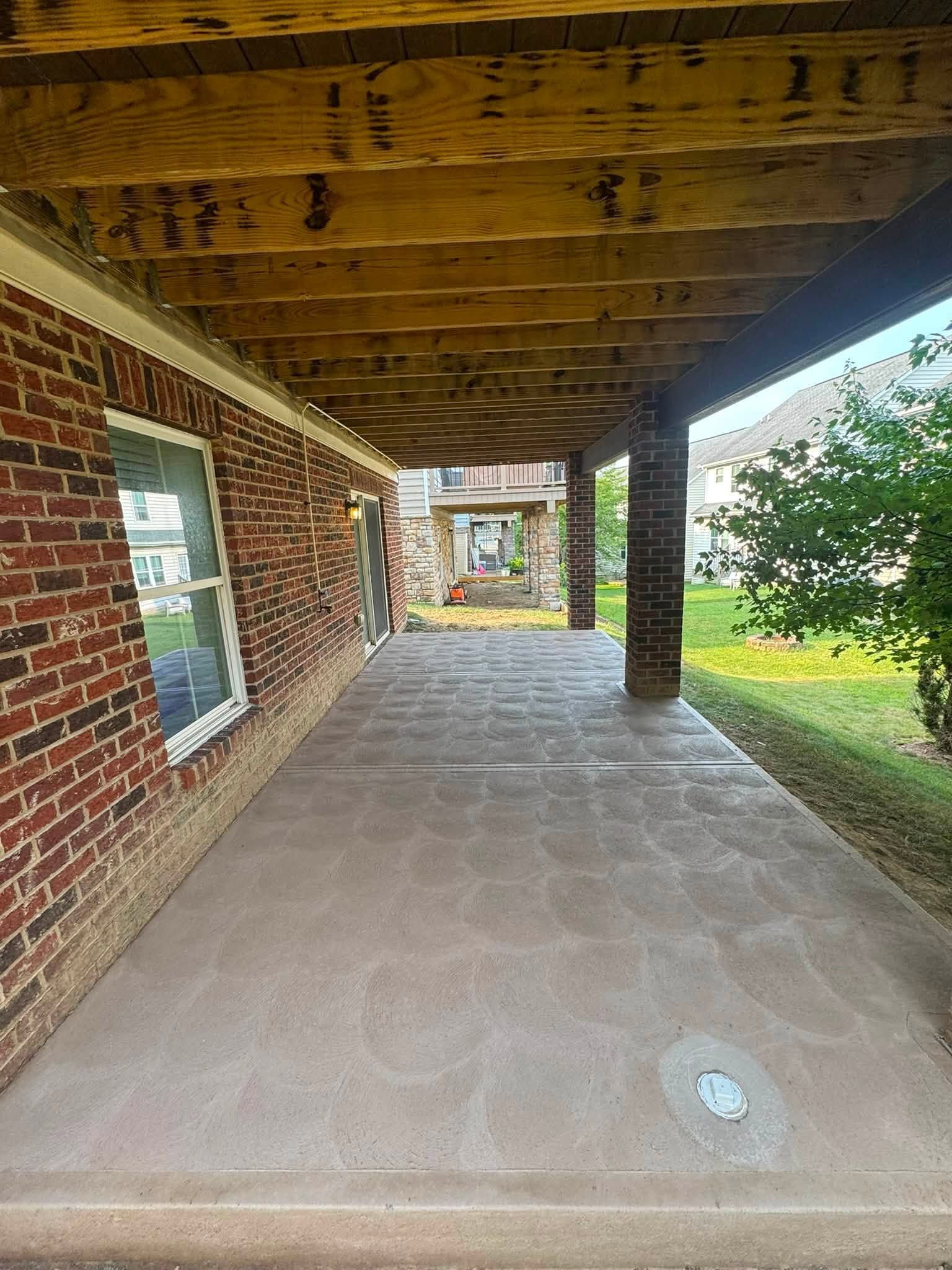 Covered brick porch with wooden beams, concrete floor, and a view of green lawn.