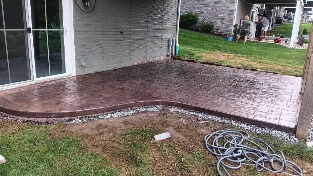 Rain-soaked backyard patio beside a house, with coiled hose and green lawn nearby.