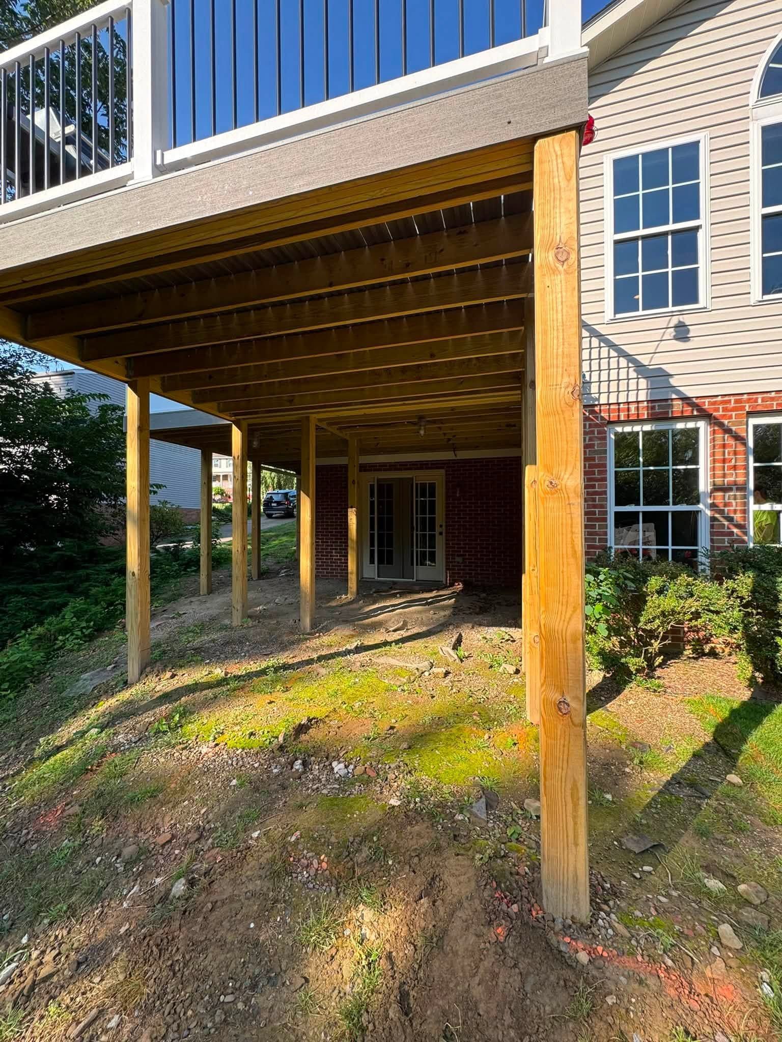 Raised deck under house with exposed wooden posts and brick exterior, overlooking a grassy yard.