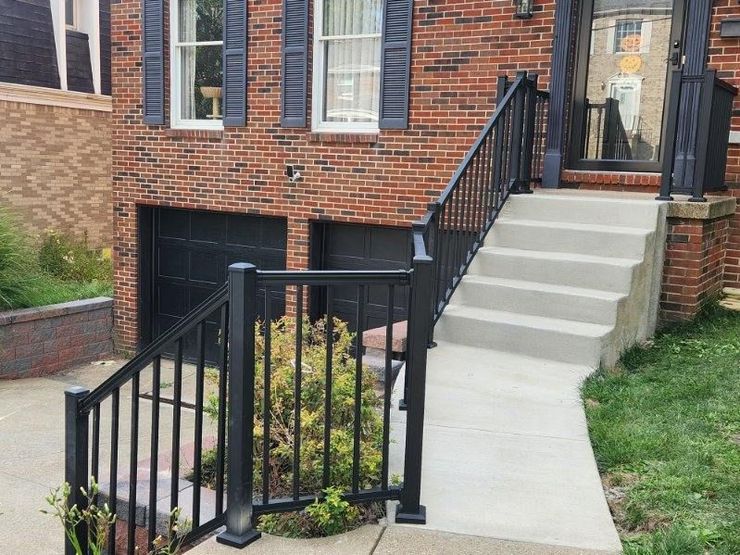 Brick townhouse entrance with concrete steps, black railings, and a small front garden