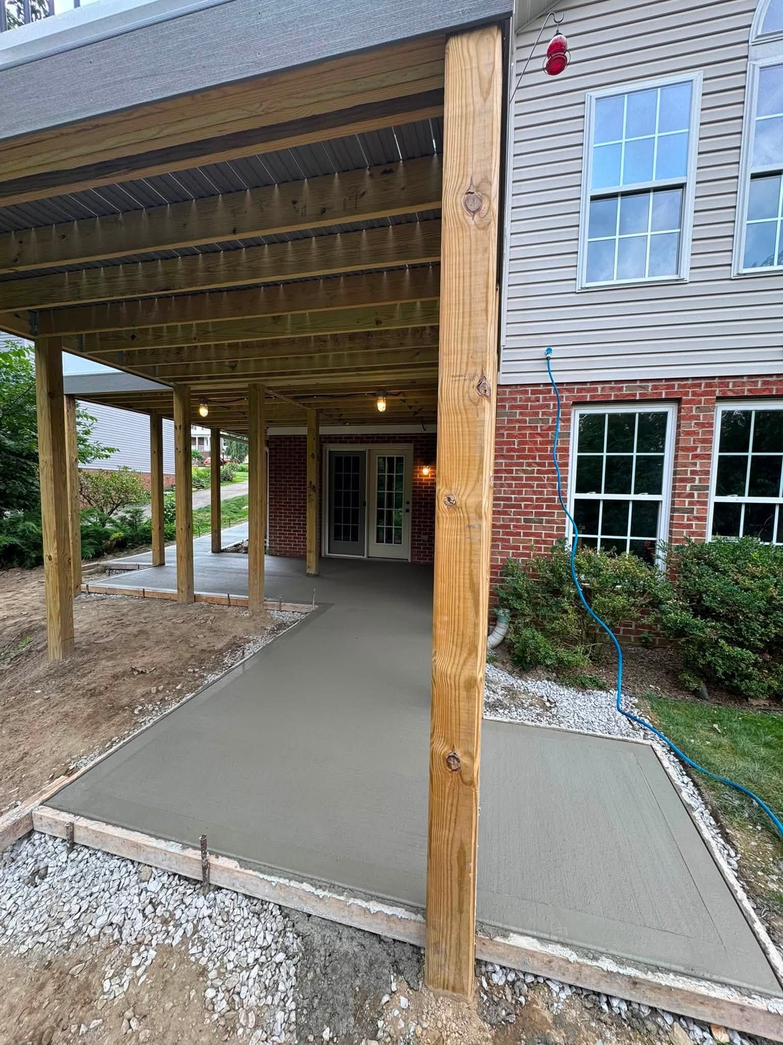 Covered building entrance with concrete walkway, wooden posts, and brick siding under a roof overhang