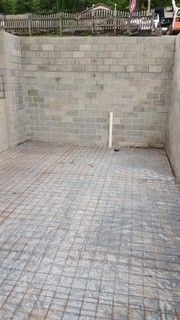 Empty paved parking area with a cinderblock wall and a white pipe near the back