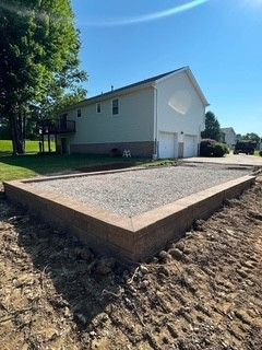 New concrete driveway beside a white house, with gravel and trees in a sunny yard