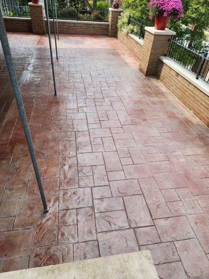 Wet brick patio with potted flowers and metal railing beside a garden path.