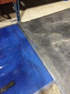Blue floor mat beside gray concrete floor near a metal shelf leg
