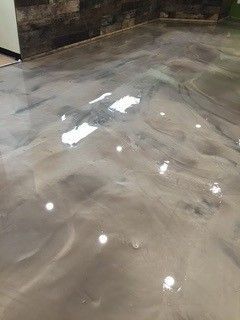 Shiny wet concrete floor with bright reflections and dark stains near a wall