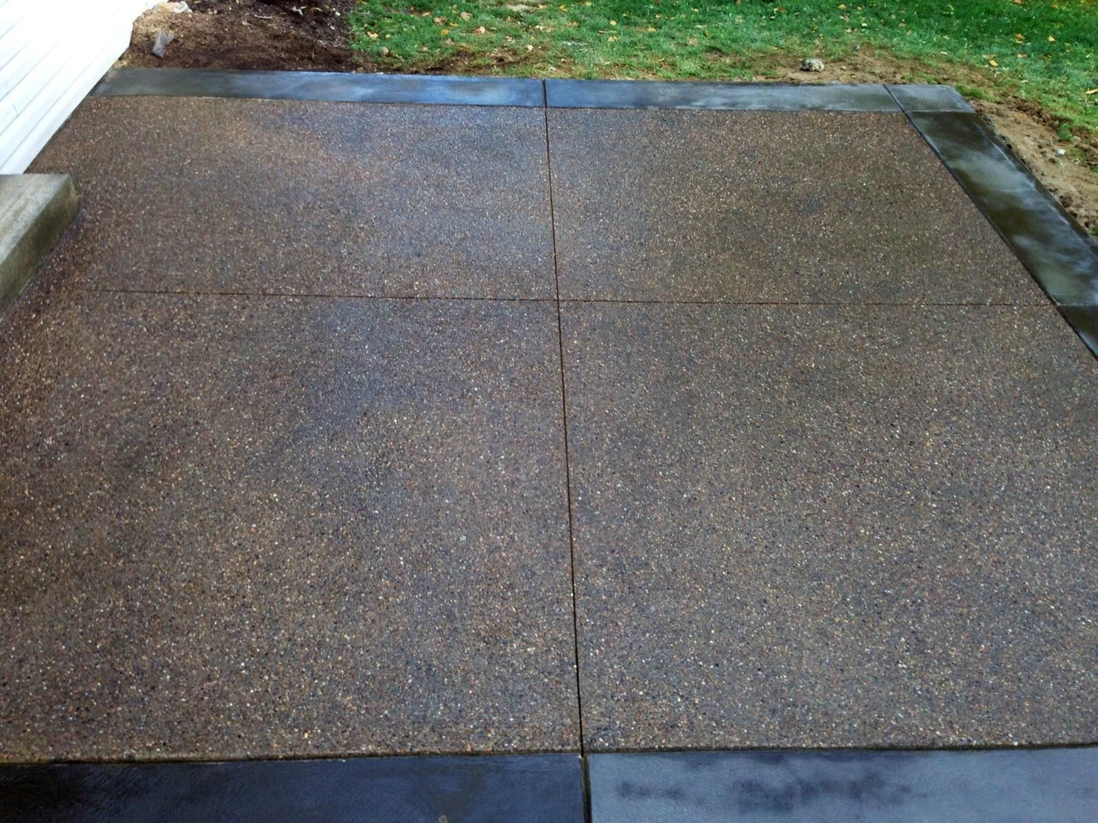 Concrete walkway with wet, dark gray paving slabs bordered by grass and soil.