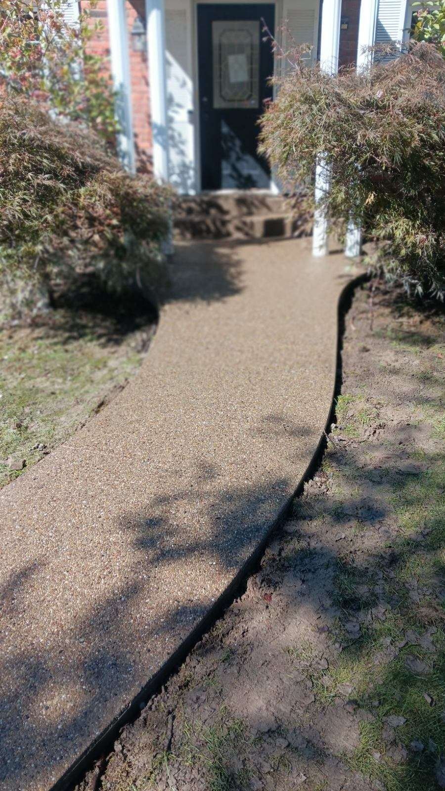 Curved concrete walkway leading to a front door, bordered by bushes and grass.
