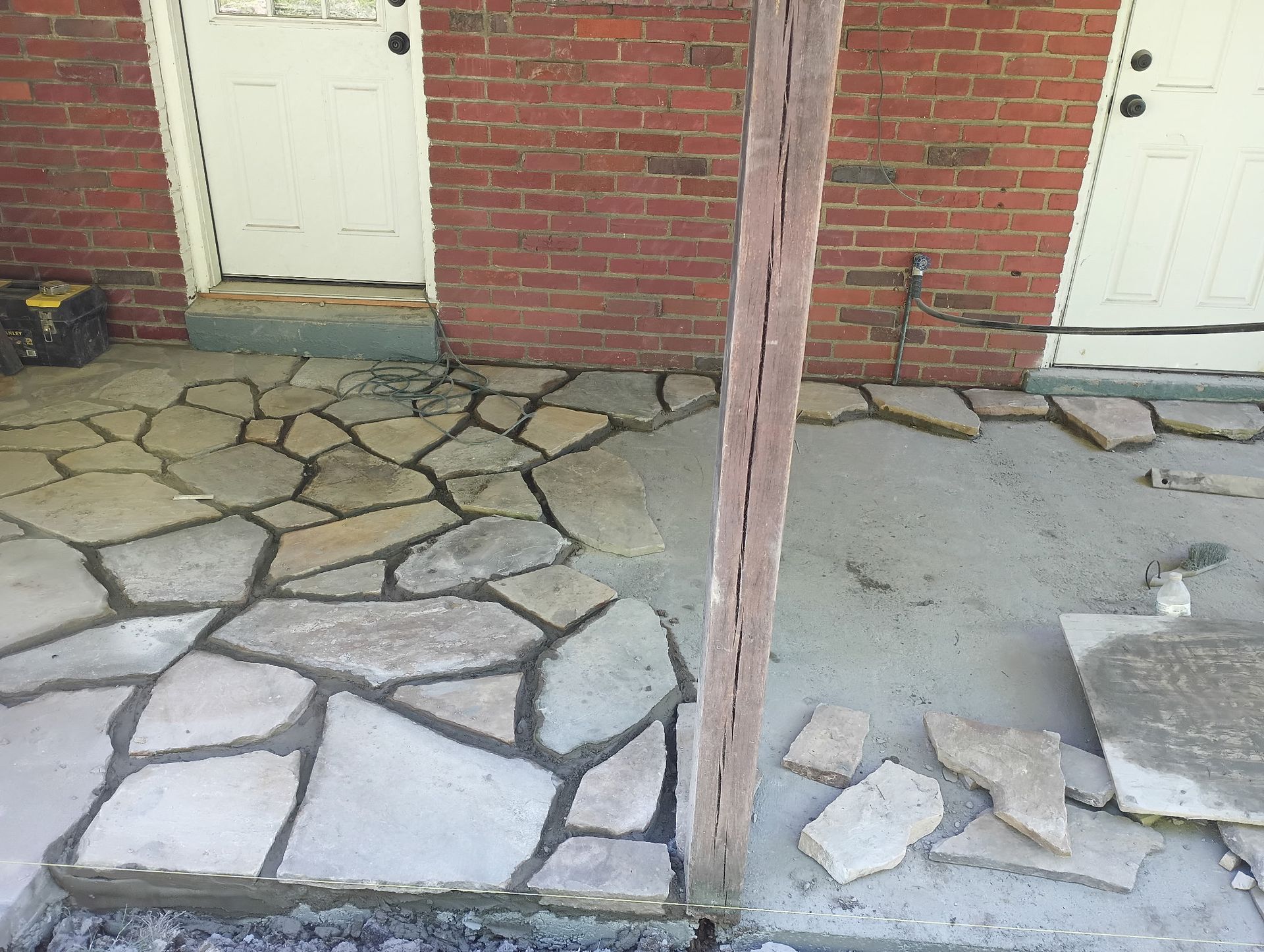 Brick building entrance with uneven stone and cracked concrete walkway, and a leaning wooden post.