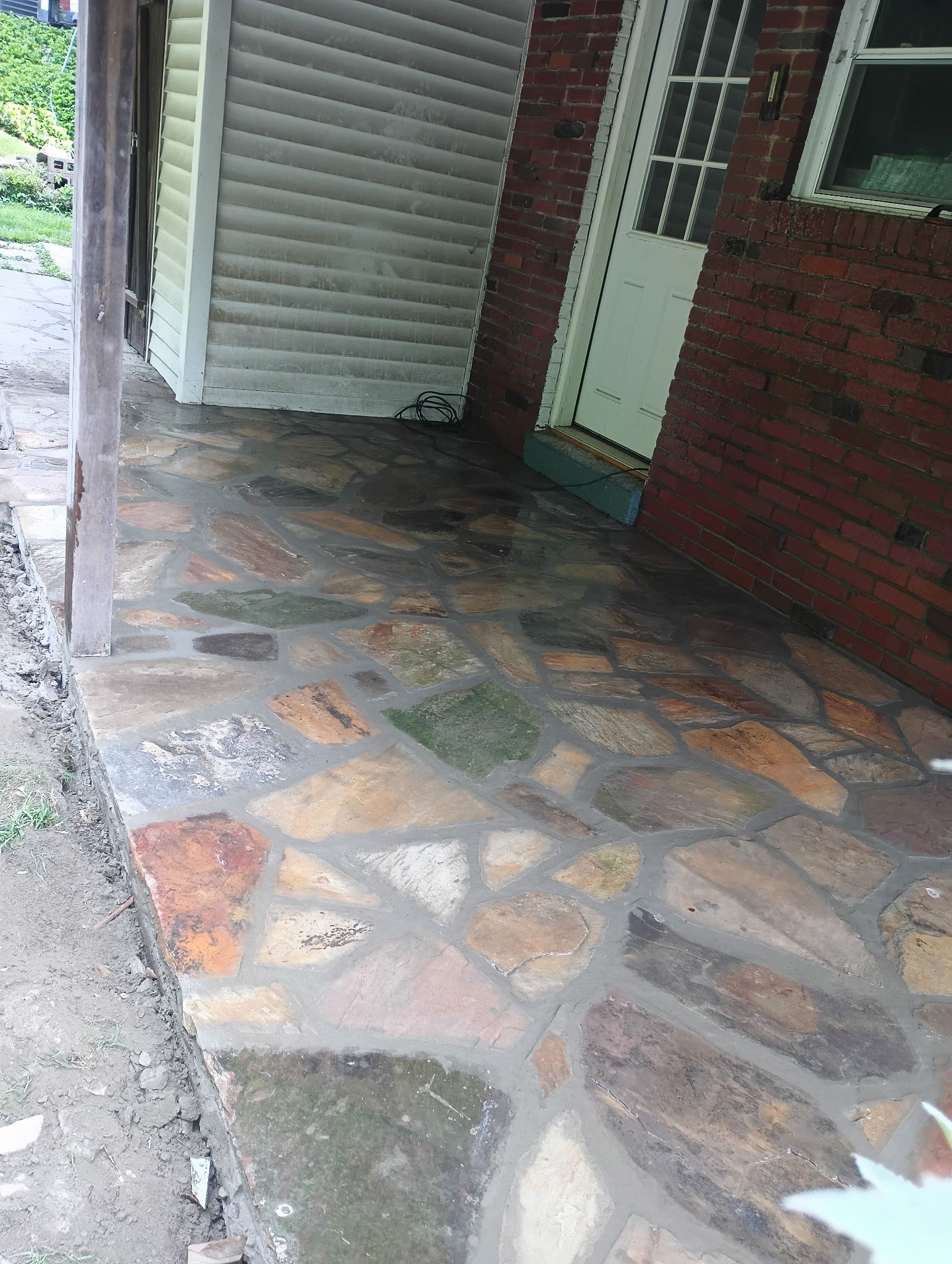 Stone porch beside a red brick wall and white siding, with a door and wet ground nearby.