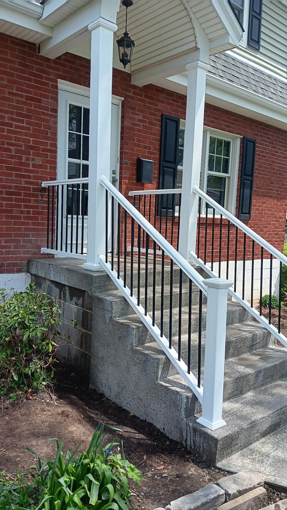 Brick house front steps with white railing and red door under a covered porch