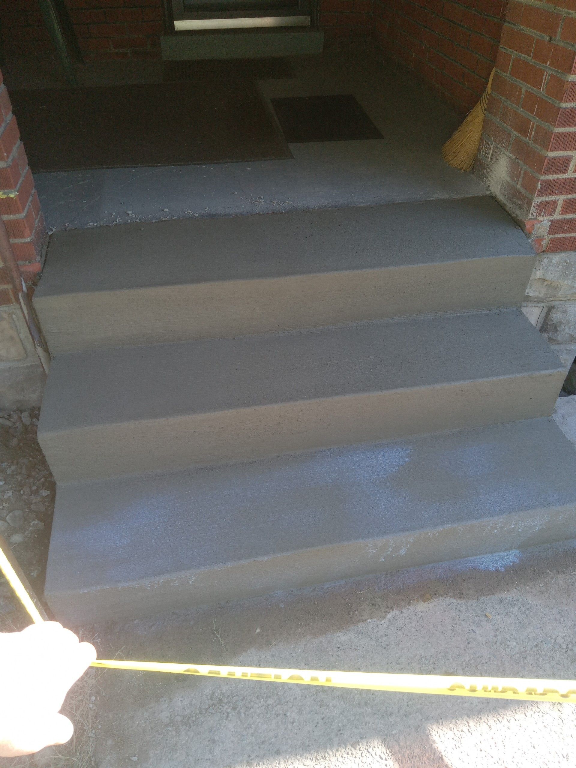 Carpeted front steps leading into a dark doorway, with a yellow measuring tape stretched across the bottom.
