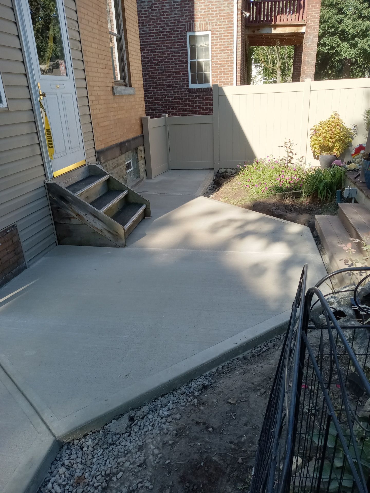 Concrete patio beside brick house with small steps, white fence, and flower bed