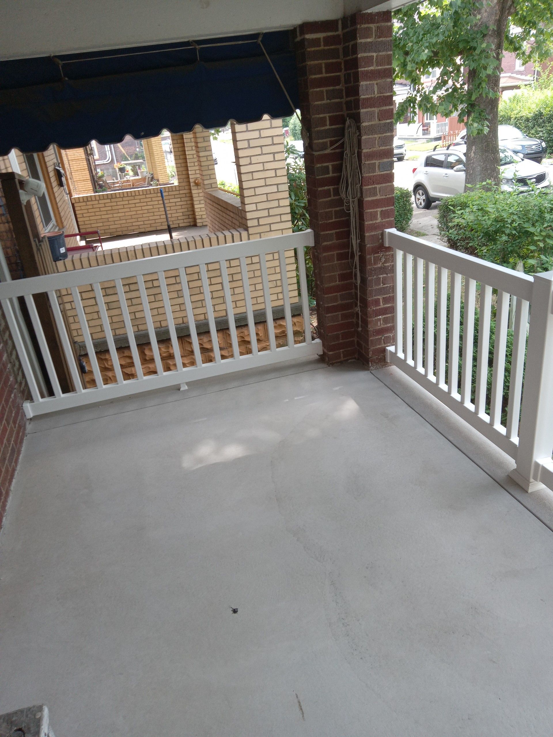 Covered front porch with white railing, brick columns, and a view of a yard and neighboring house.