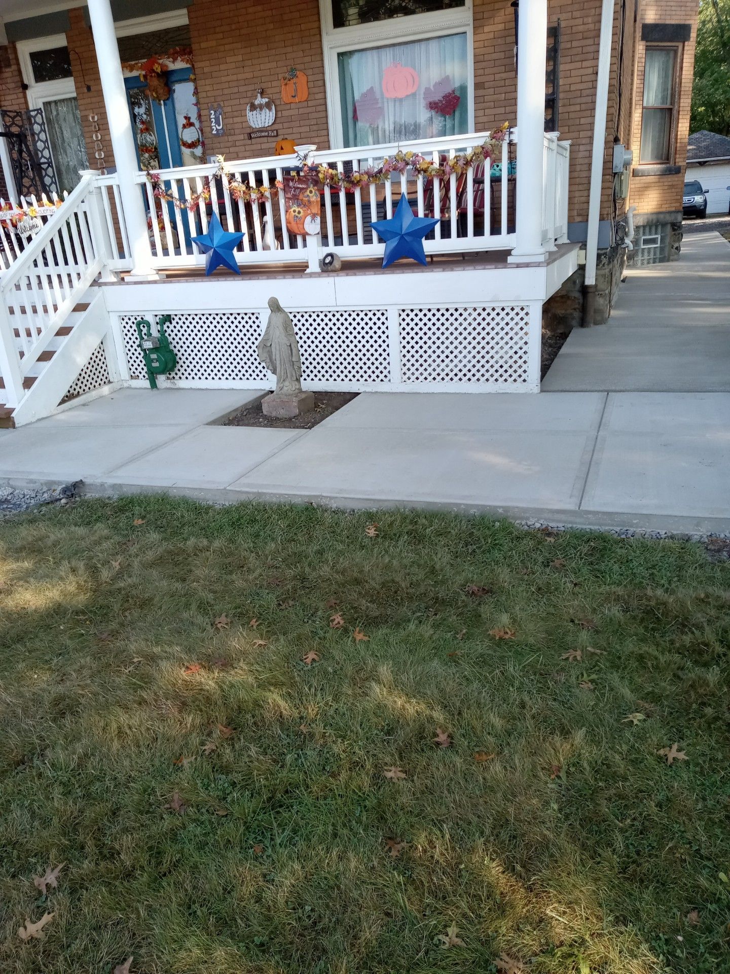 Front porch with white railing, blue chairs, concrete sidewalk, and a grassy lawn in front of a brick house