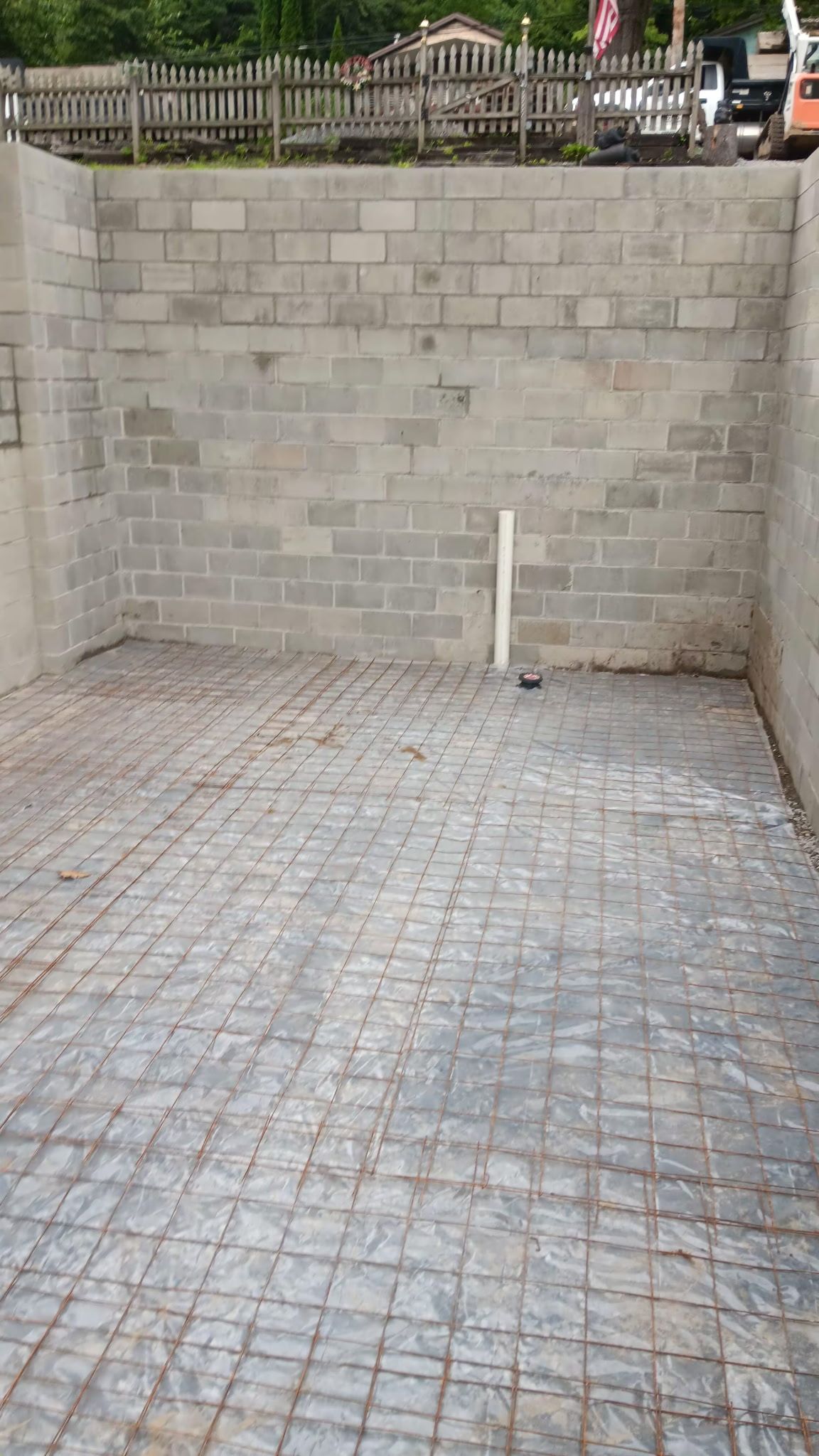 Empty concrete-block walled courtyard with a paved floor and a white pipe near the back wall.