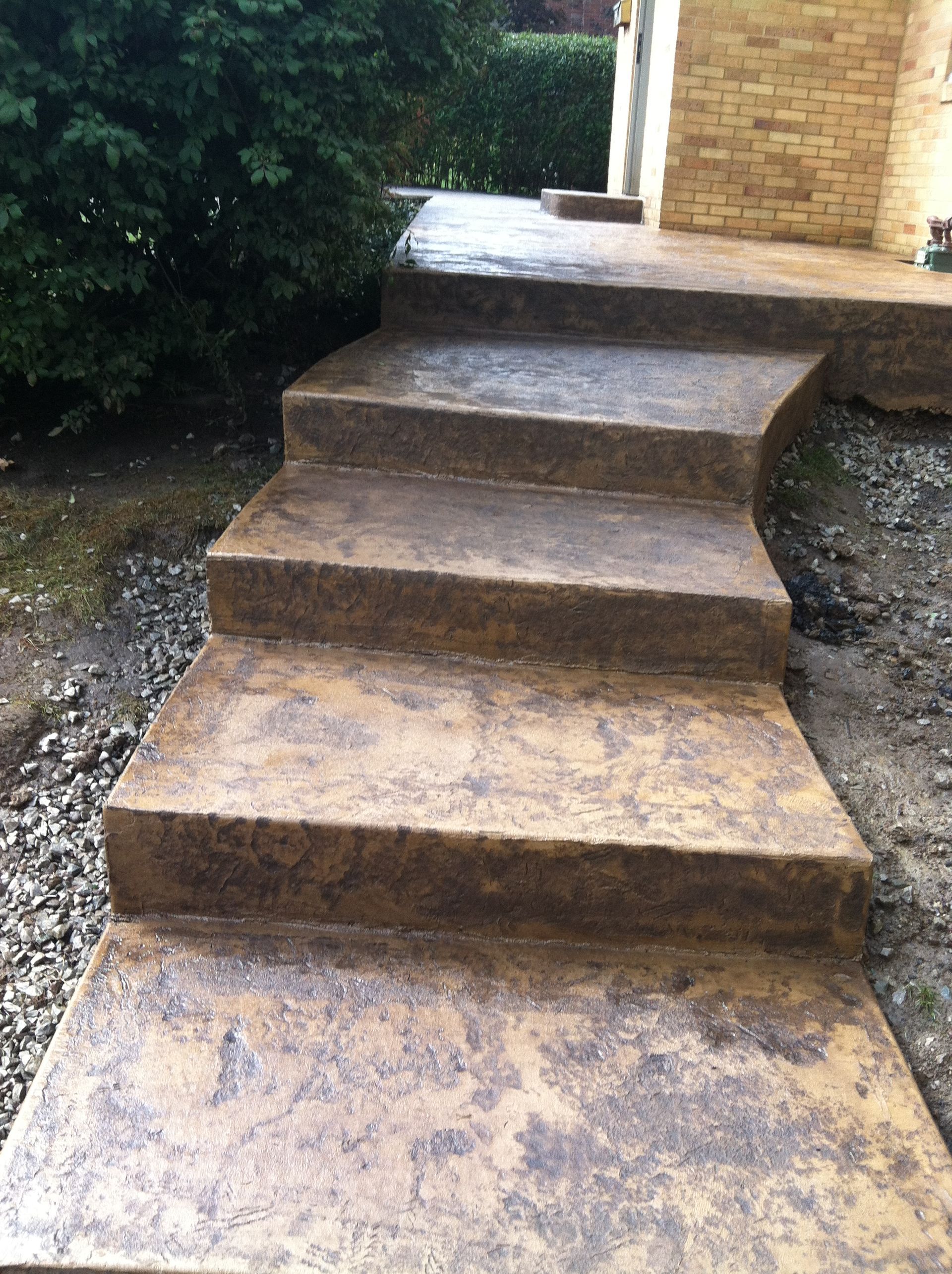 Rustic stone steps leading up to a house entrance beside bushes and gravel path.