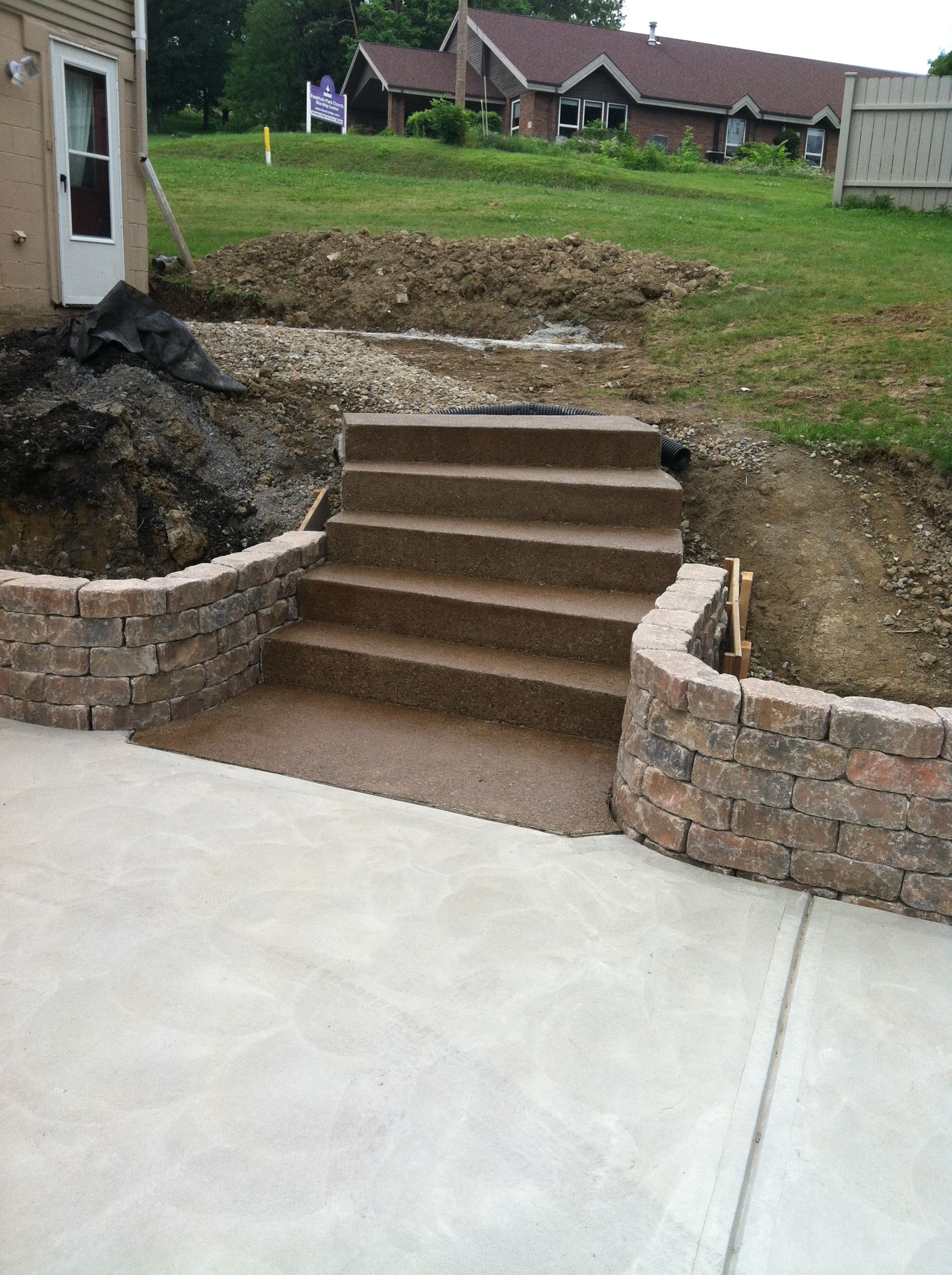 Stone steps leading from a concrete patio up to a grassy backyard with retaining walls on both sides
