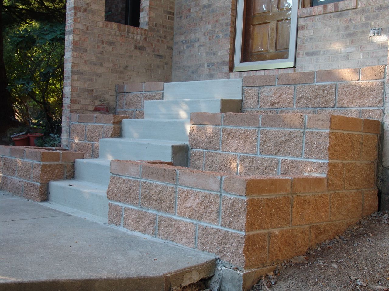 Brick steps beside a concrete walkway leading to a building entrance with a wooden door.