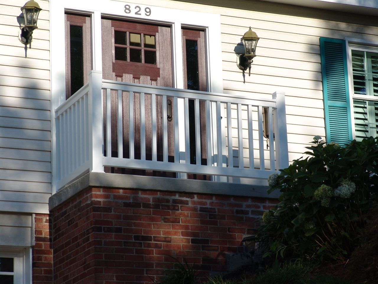 Front porch with white railing, red door, and house number 829 on a brick-and-siding home