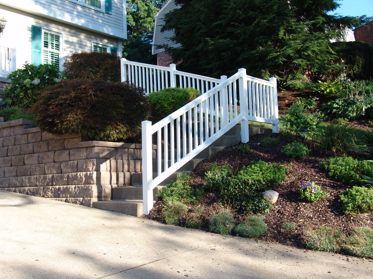 White railing staircase beside a brick retaining wall and landscaped shrubs by a house