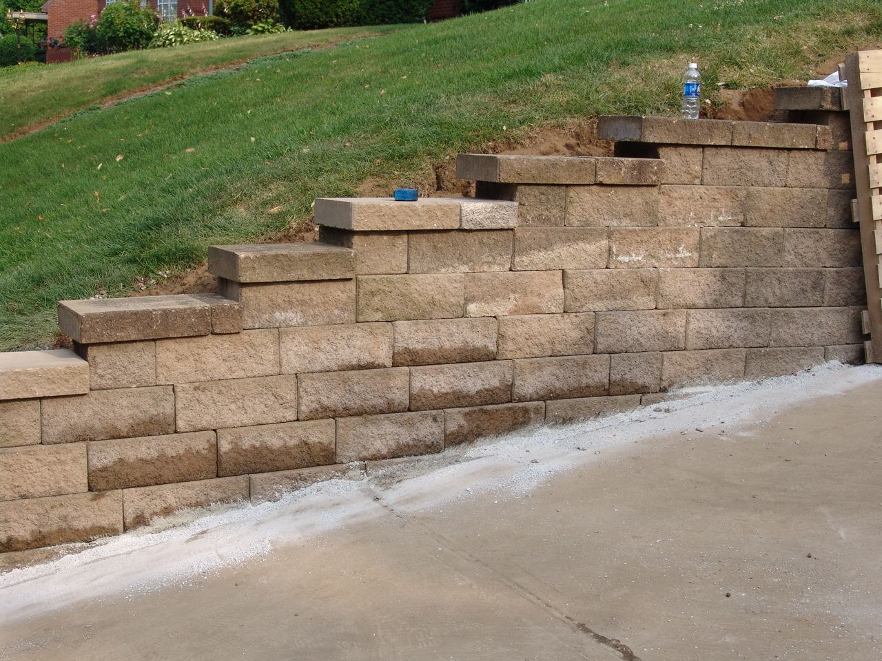 Tan retaining wall with steps beside a sloped grassy yard and concrete driveway