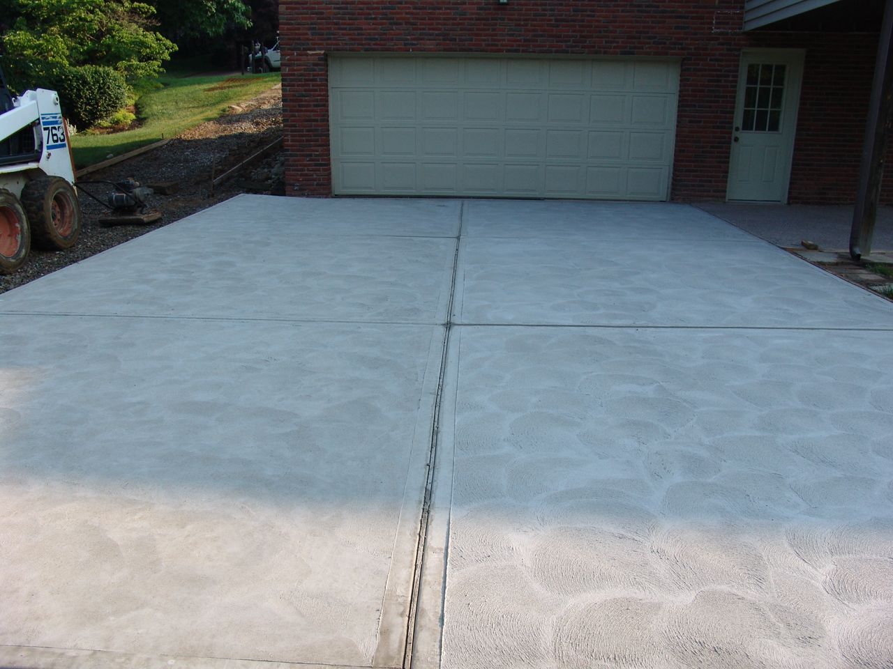 Concrete driveway leading to a garage on a brick house, with a center expansion joint line.