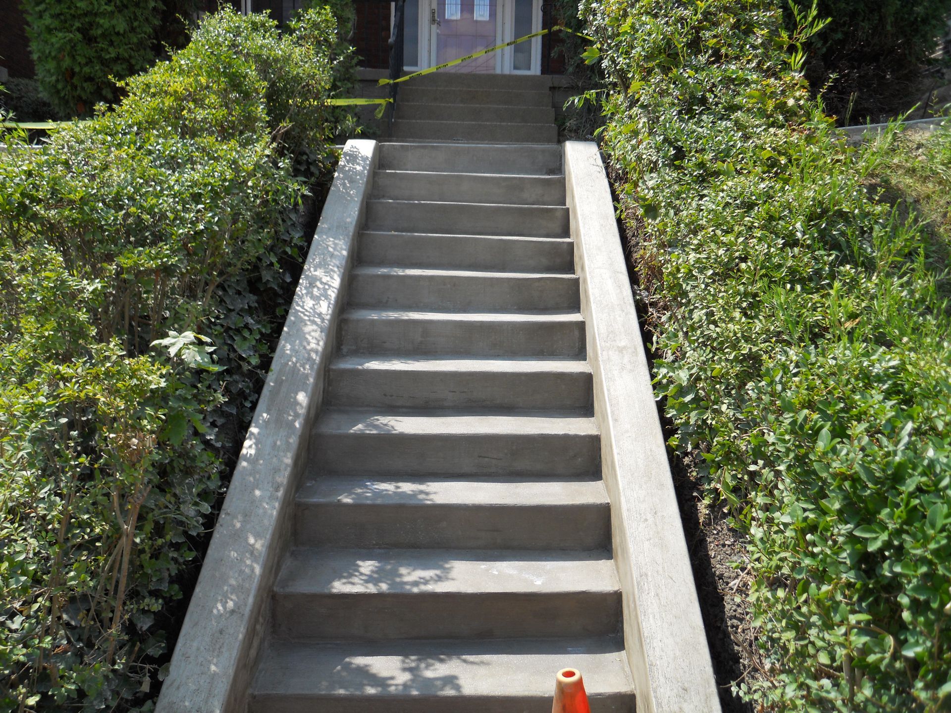 Concrete outdoor staircase lined with bushes leading up to a house entrance