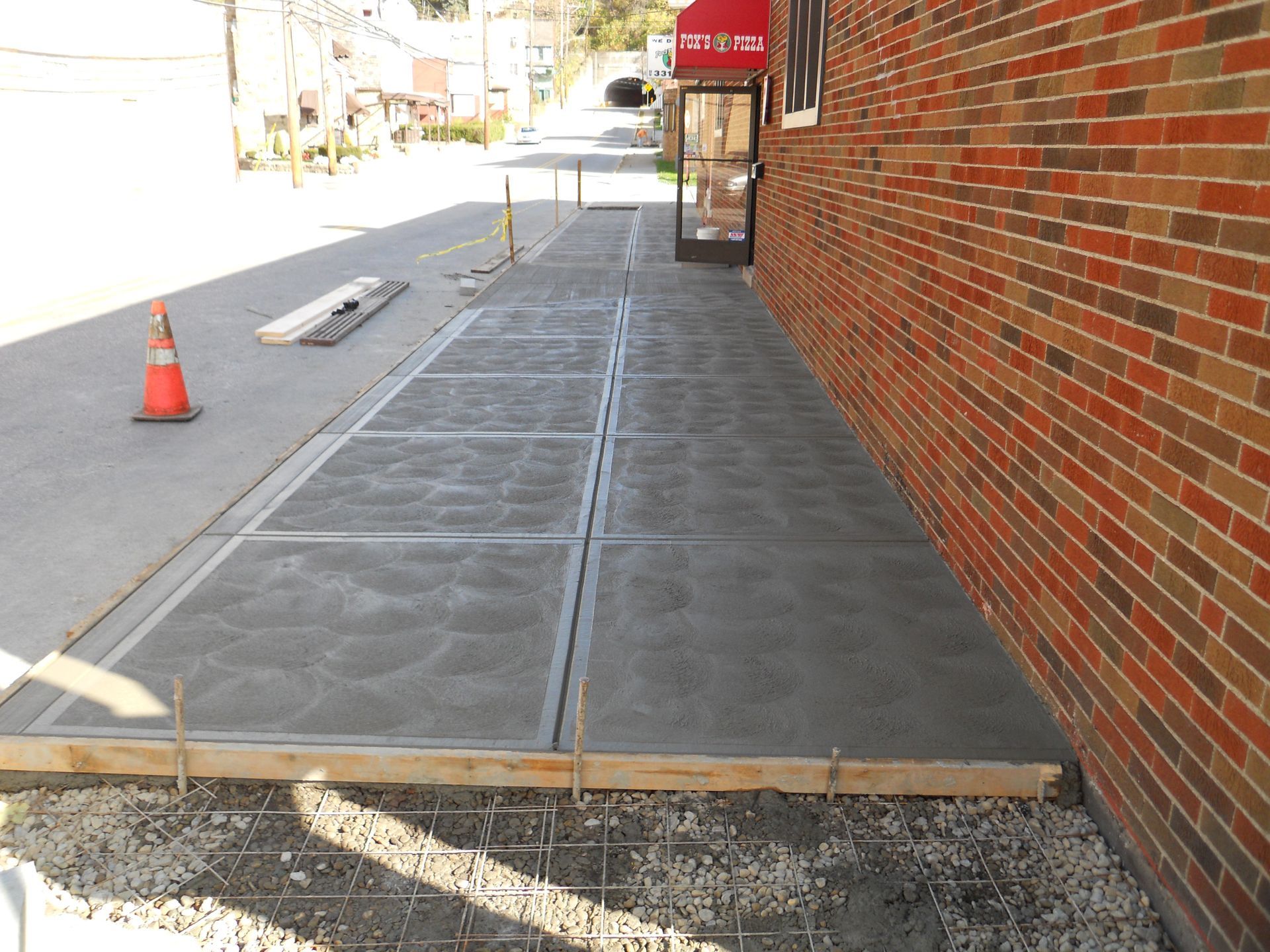 Temporary black sidewalk ramp beside a brick building, with an orange cone on the street.
