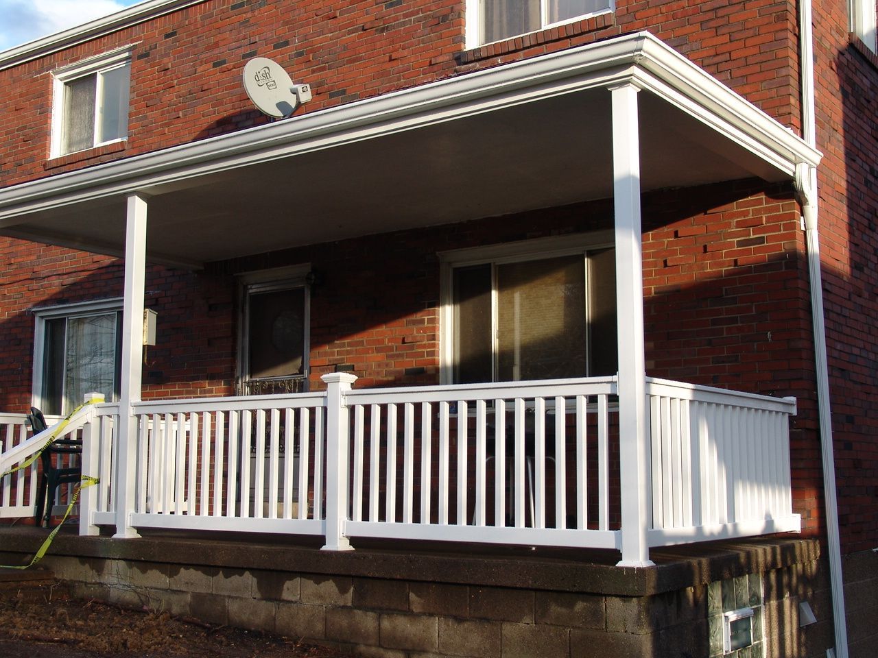 Red brick house with a white porch and railing, front steps, and a satellite dish on the facade