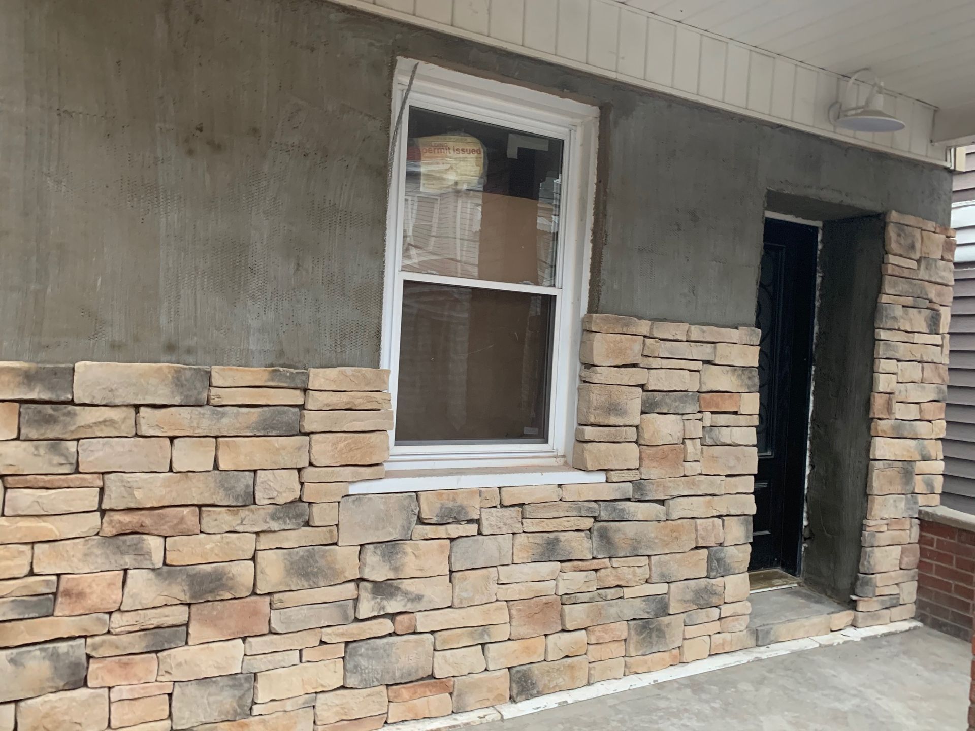 Partially renovated house exterior with stone veneer, window, and open doorway