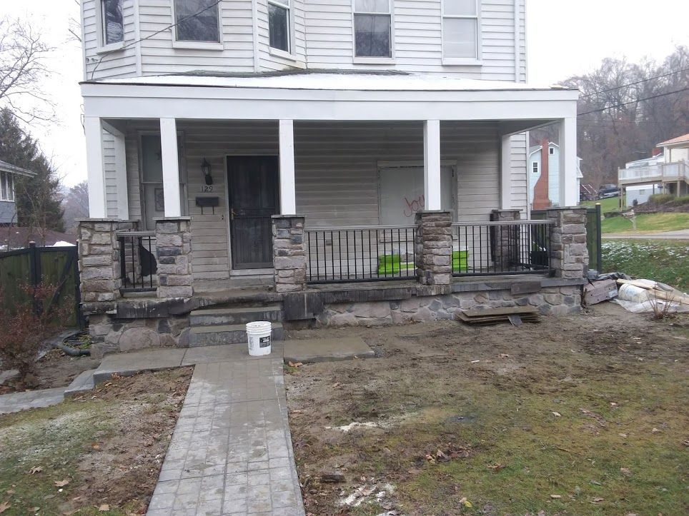 Front porch of a white house with black metal railings and a wet stone walkway leading up to it.